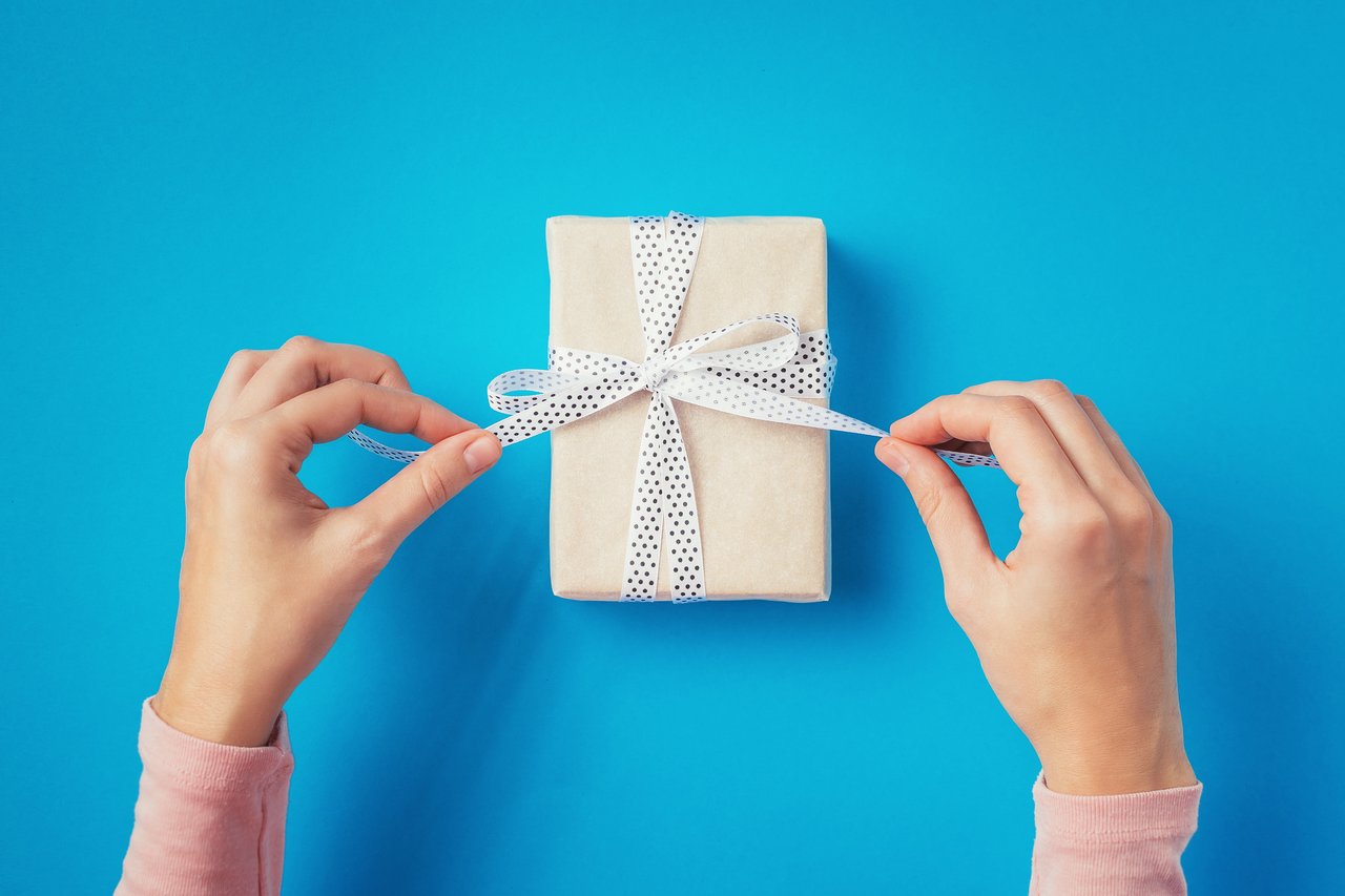 woman hands untie bow on gift box on blue background, top view